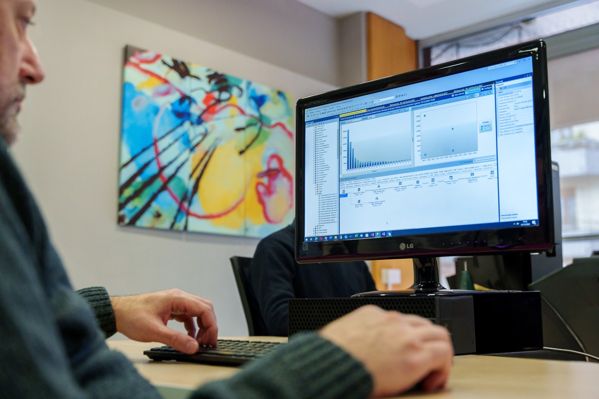 Professionista al lavoro su software di analisi dati in ambiente ufficio, con grafici visibili sullo schermo