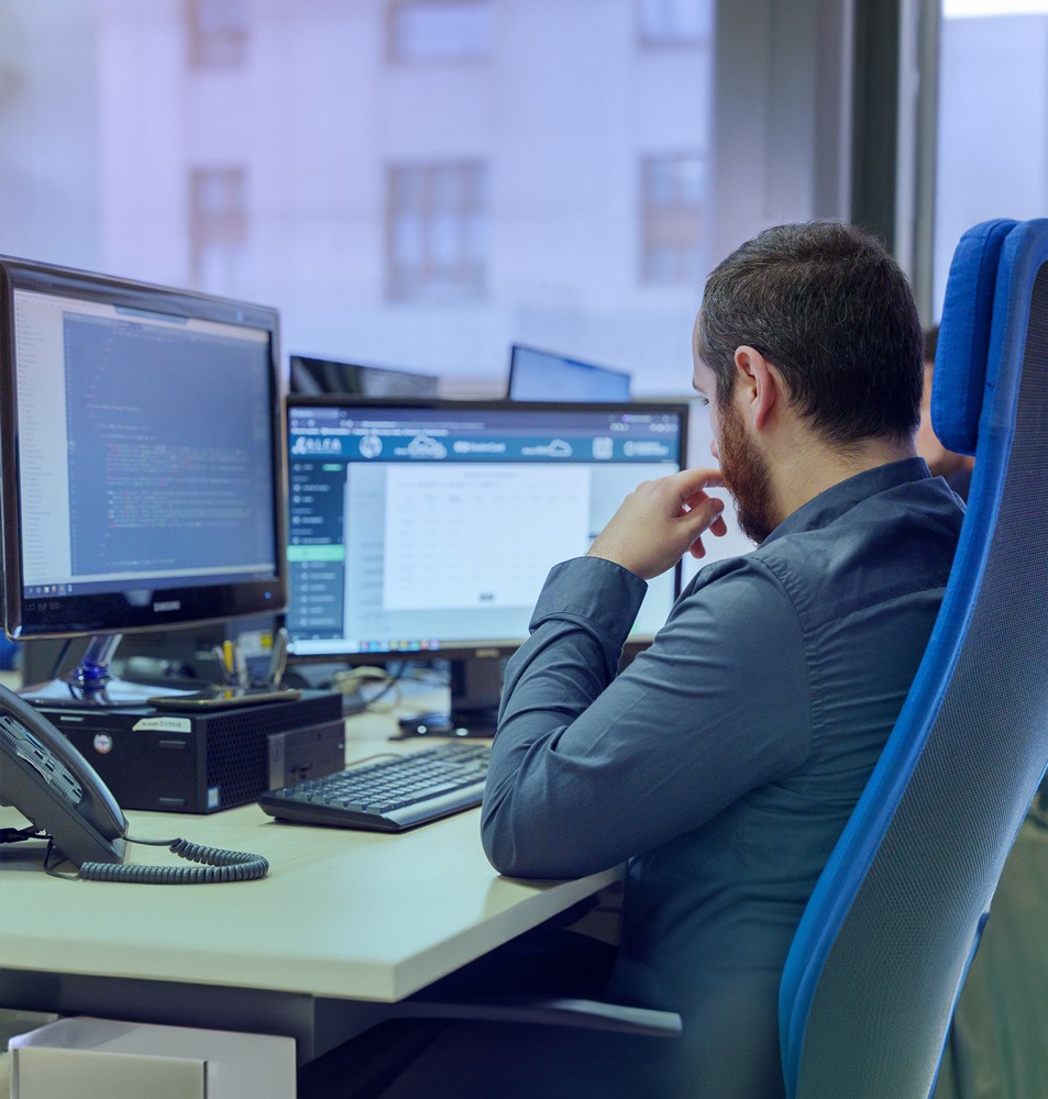 Tecnico informatico al lavoro su doppio monitor con codice e interfaccia della piattaforma Dealer Suite